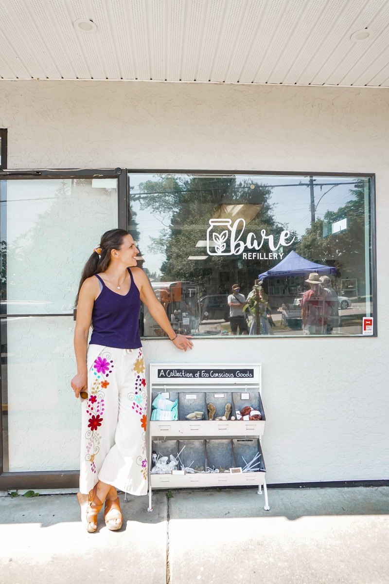 Woman standing outside the Bare Refillery storefront beside a goods display