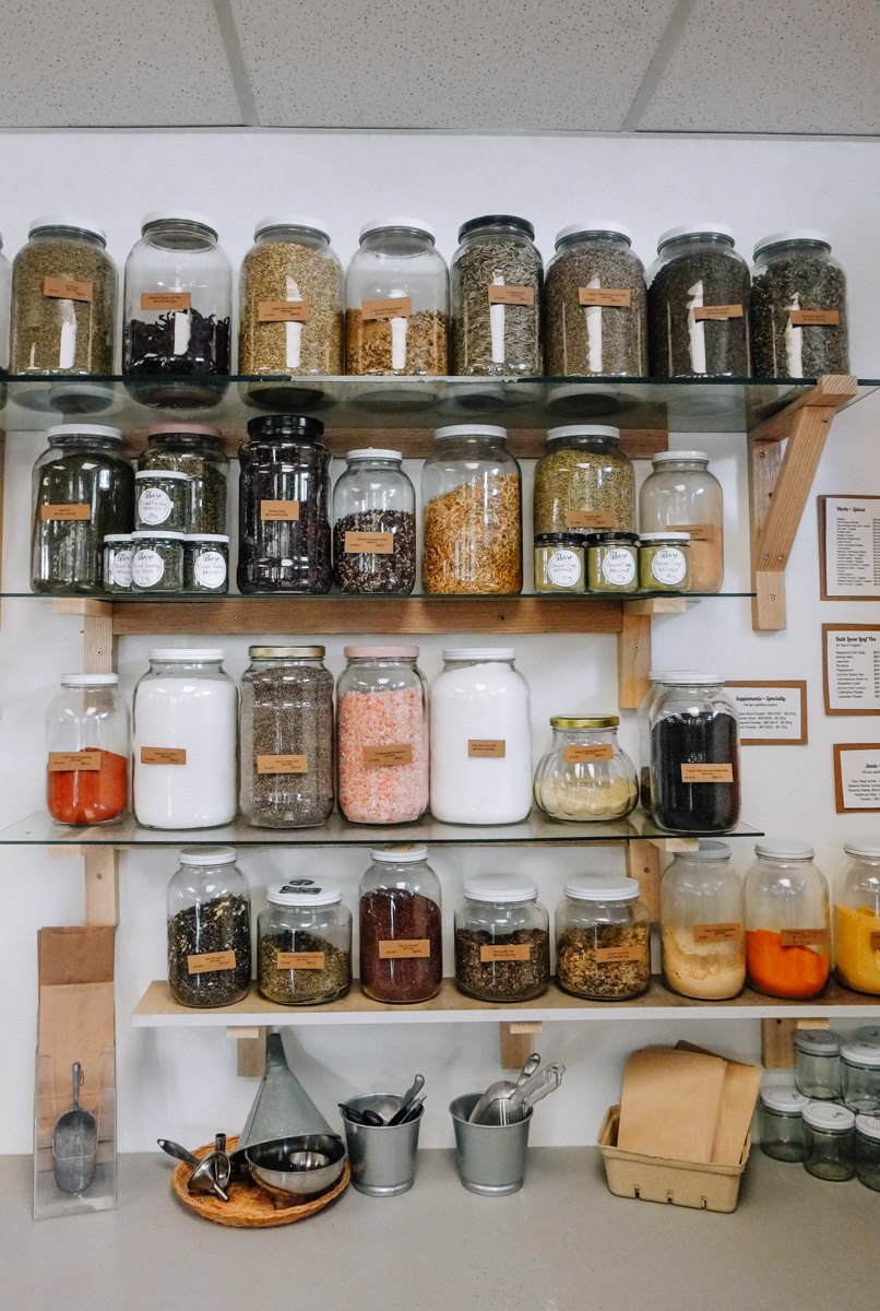 Glass jars of teas, spices and salts on wooden refill shelves