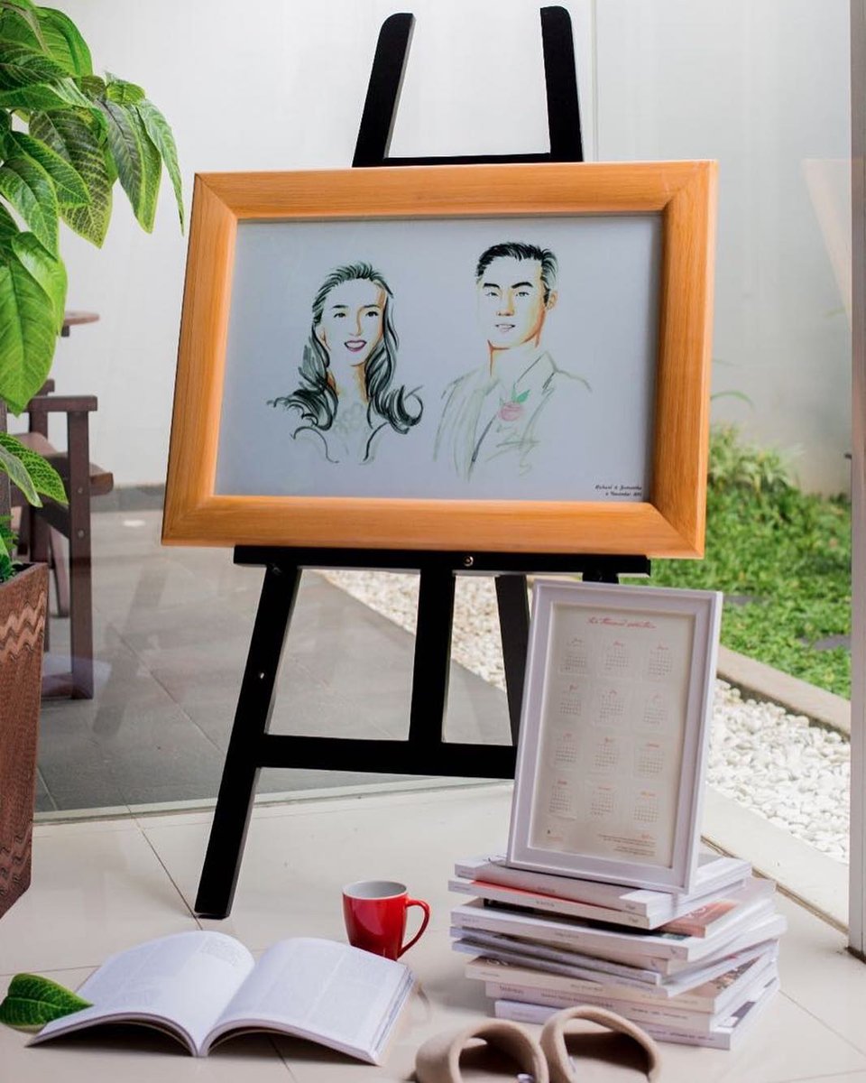 Framed illustrated couple portrait on an easel with a guest book and photobooks