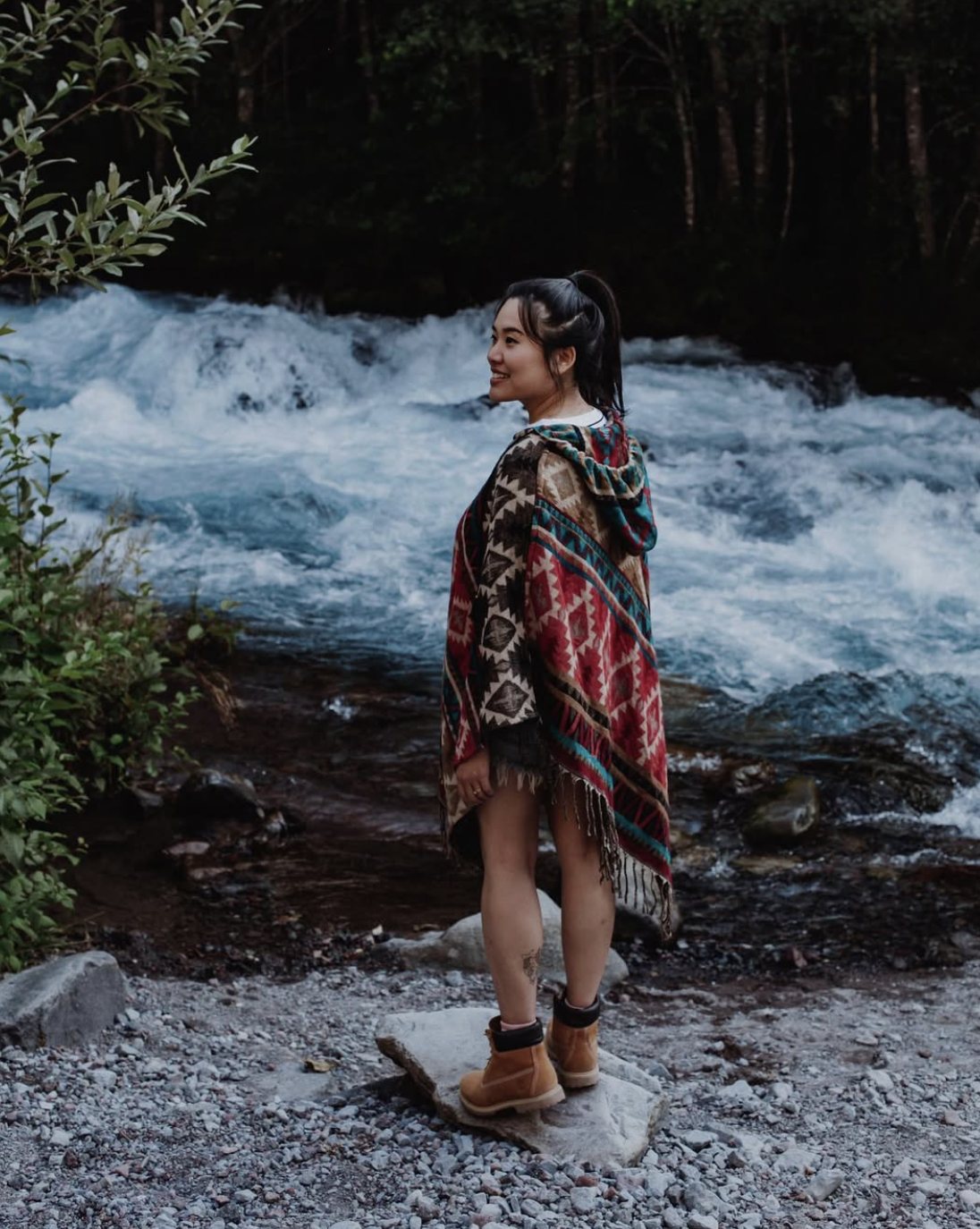 Gita standing by a river in a patterned poncho